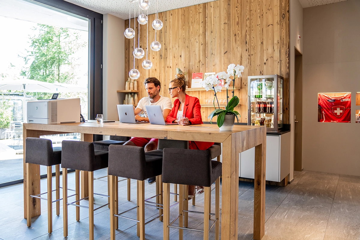 Ein Mann und eine Frau sitzen am Hochtisch mit ihren Laptops und vergleichen die Angebote