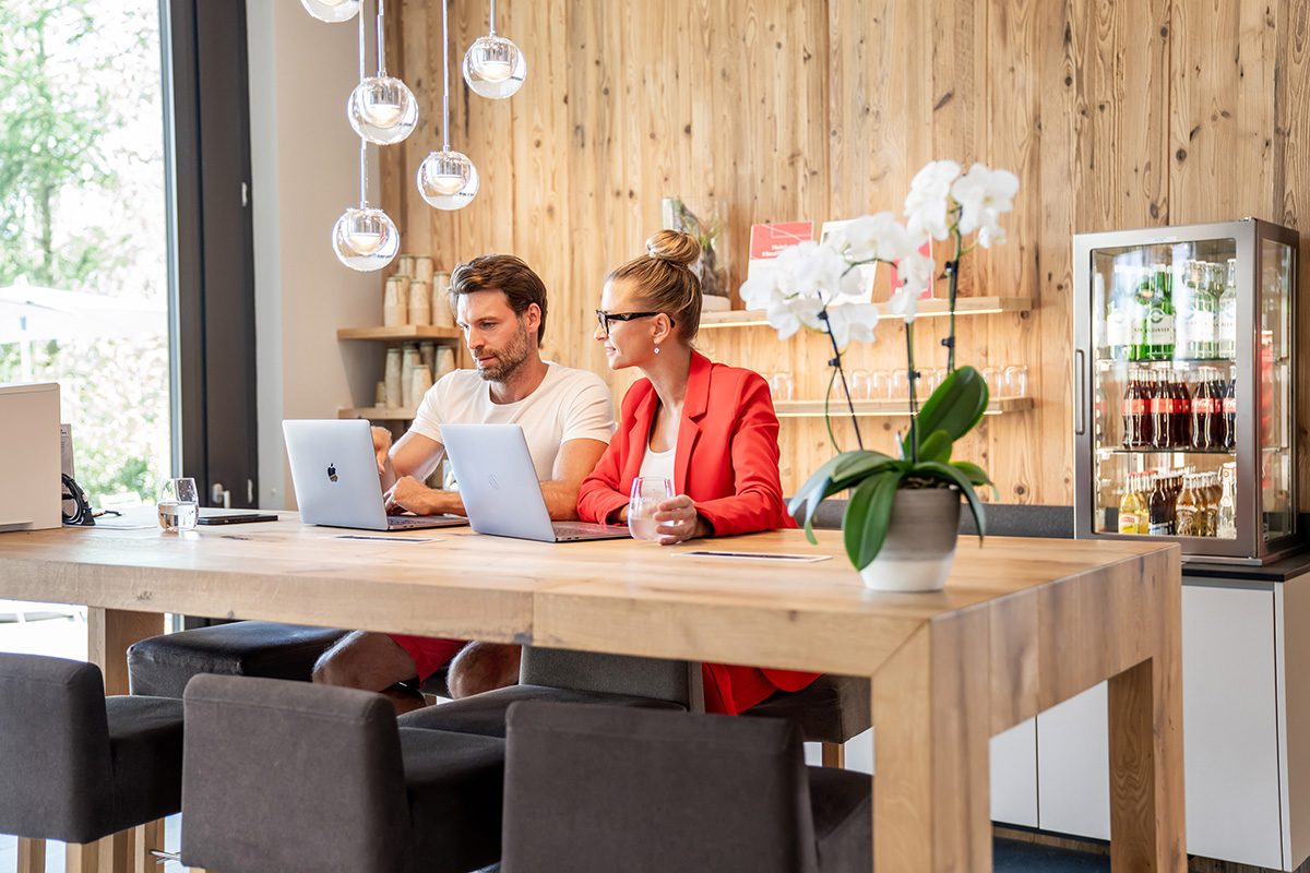 Ein Mann und eine Frau sitzend am Hochtisch mit ihren Labtops am Angebote vergleichen