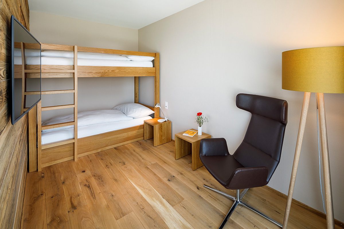 Lodge Suite, Kinderbereich, Hotel Allegra Lodge, Etagenbett mit zwei Nachttischen und ein Relaxsessel mit Stehleuchte, an der Wand ein TV-Gerät montiert