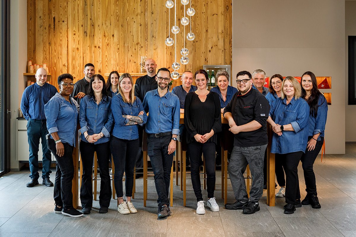 Team, Hotel Allegra Lodge, Personal Männer und Frauen mit blauen Jeanshemden, Köche mit schwarzer Uniform stehend vor dem Hochtisch beim Hoteleingang