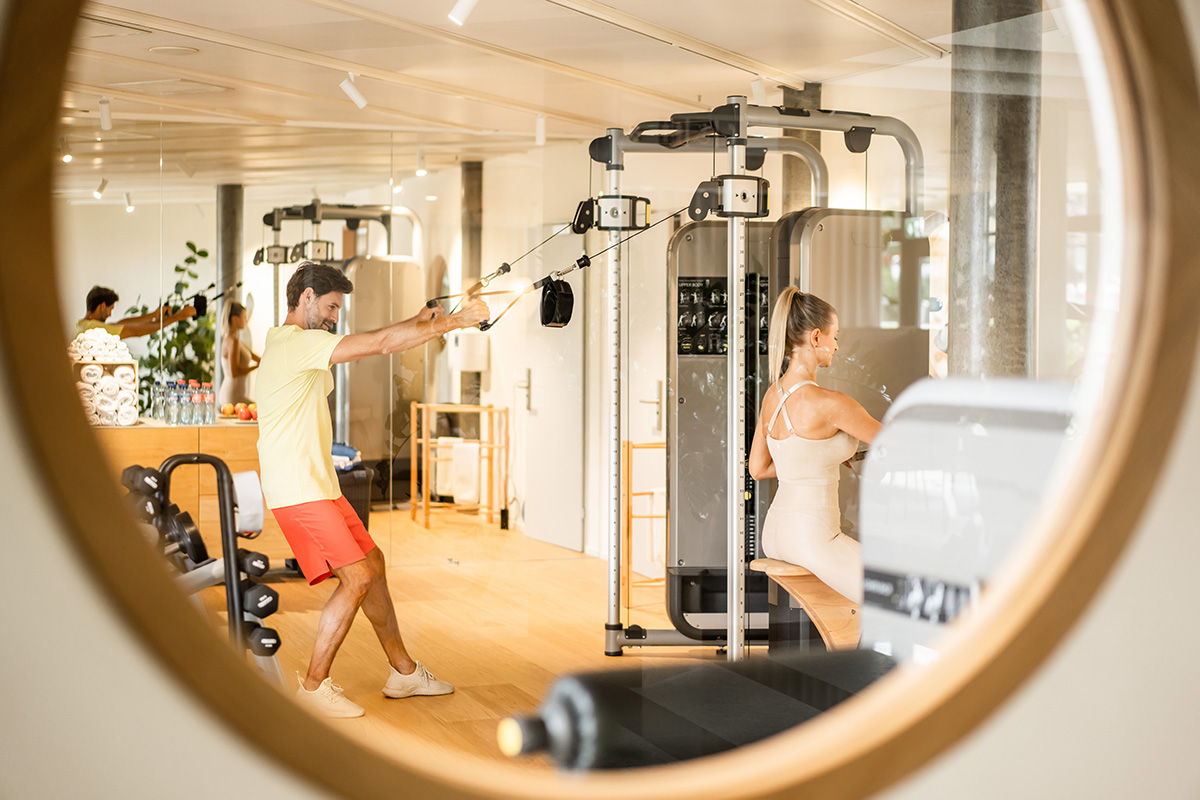 Eine Frau und ein Mann trainieren im Gym der Allegra Lodge und sind durch ein Fenster zu sehen.