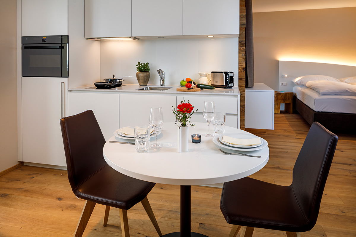 Moderne, voll ausgestattete Küche im achesa homes Serviced Apartment mit Esstisch, Parkettboden und Blick in das Schlafzimmer.