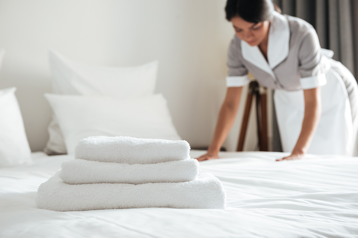 Mitarbeiterin macht das Gästebett und im Vordergrund sind Handtuecher zu sehen.