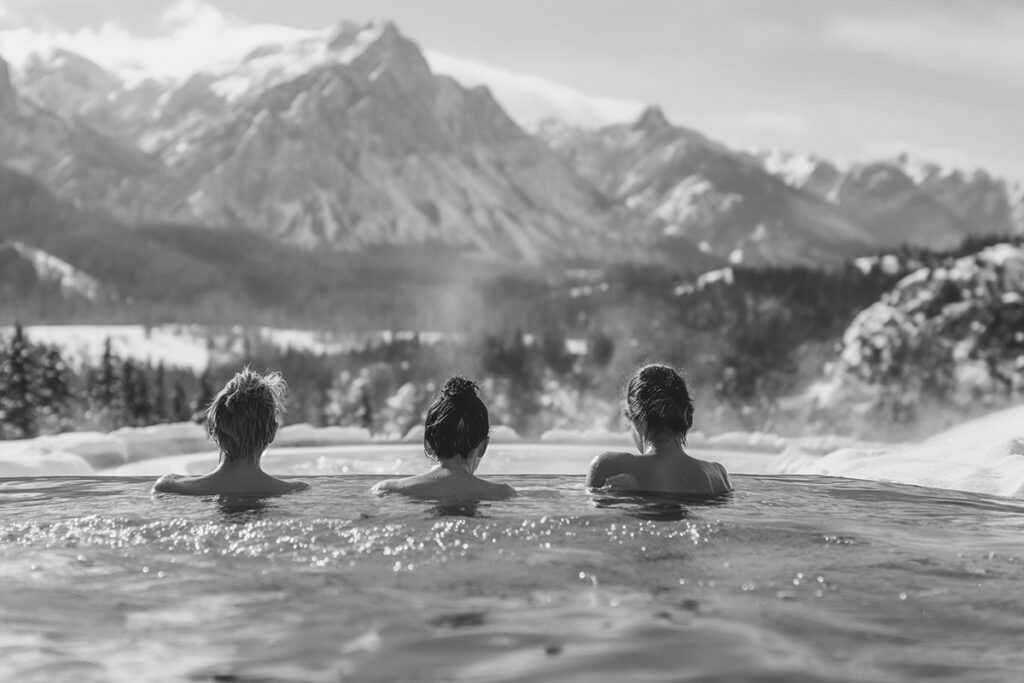 Drei Frauen sitzen im dampfendem Wasser und betrachten die Berge im Winter.