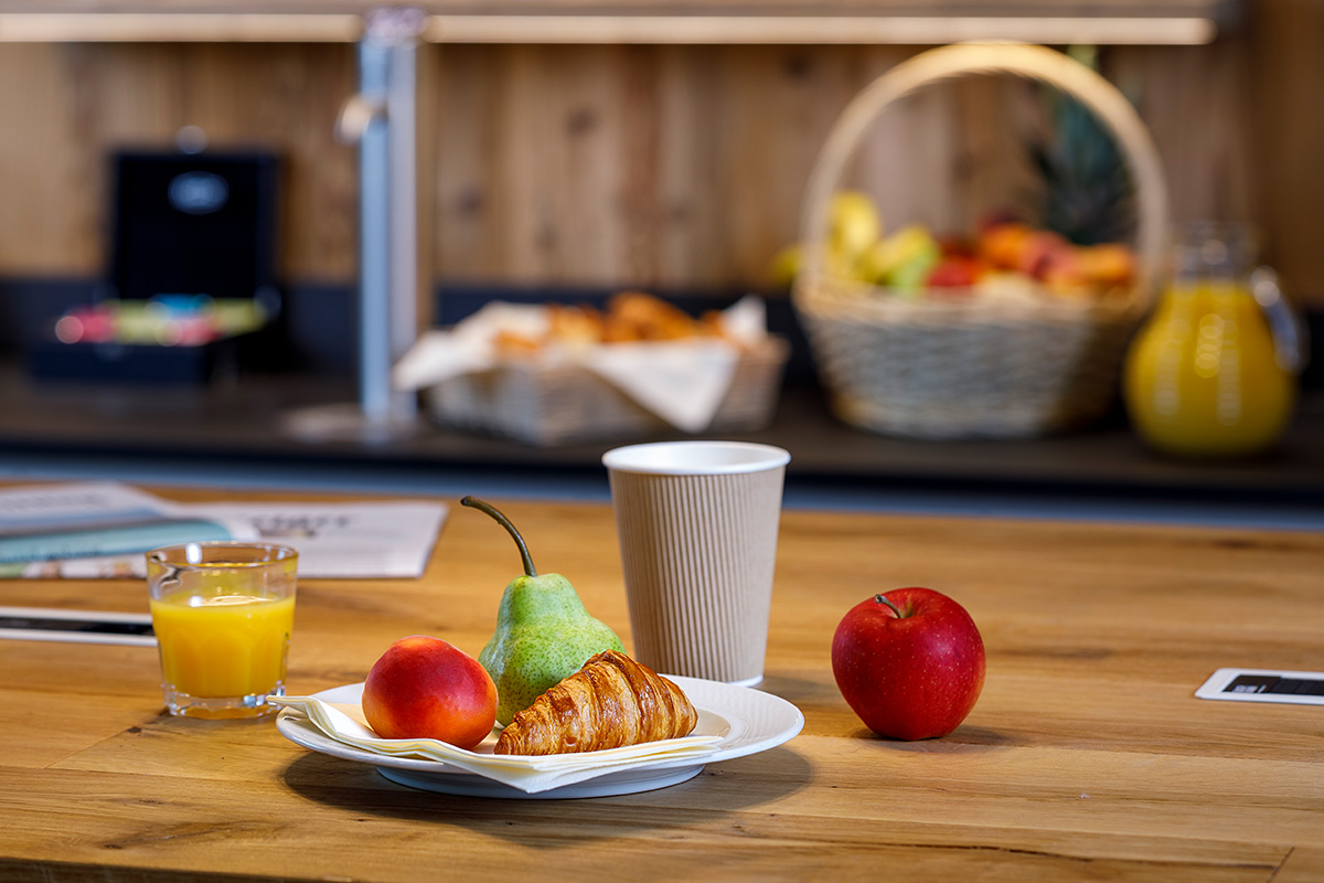 Express breakfast at Allegra Lodge with coffee, a croissant, and fresh fruit on a wooden table.