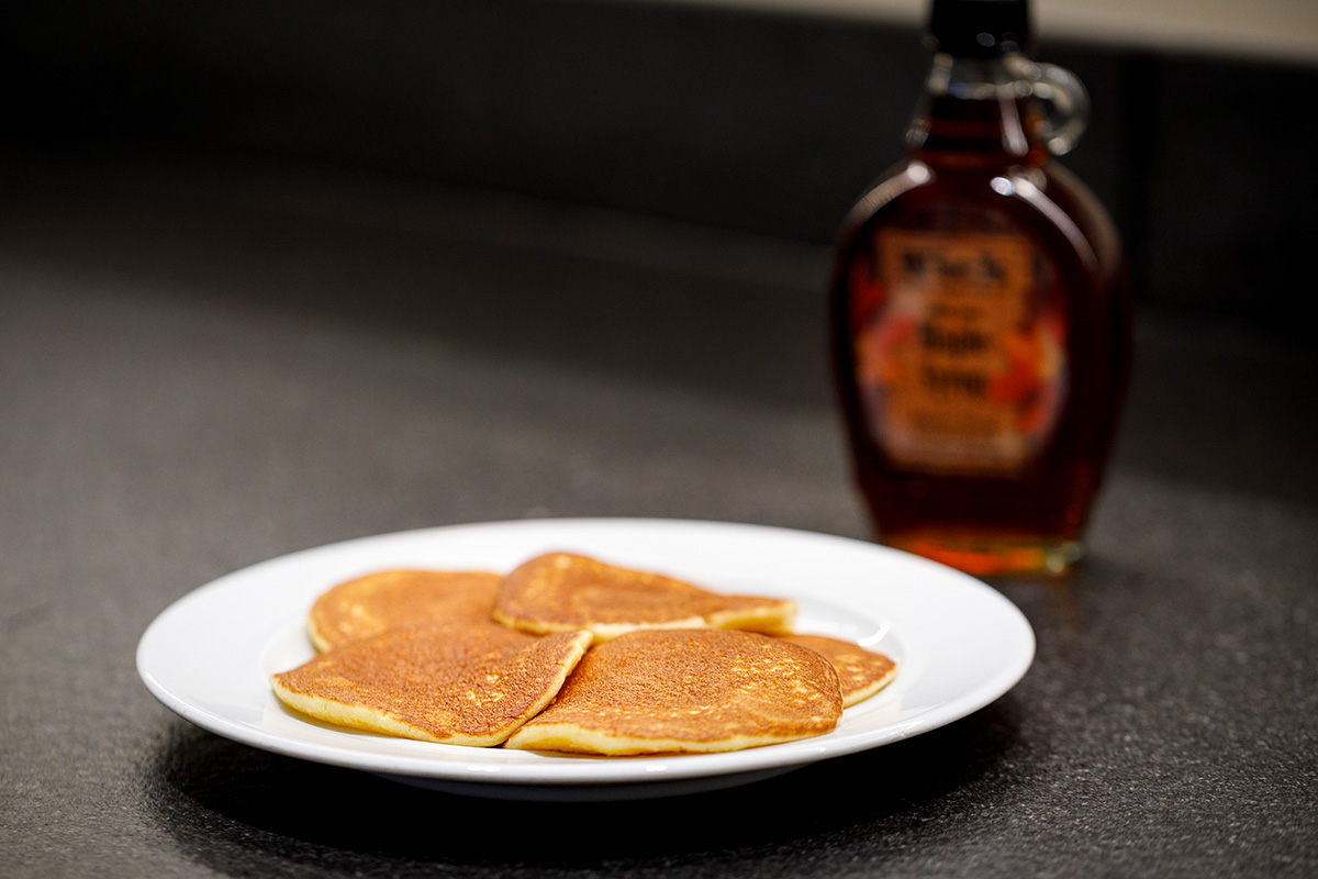 Golden-brown pancakes on a white plate with maple syrup in the background at the breakfast buffet.