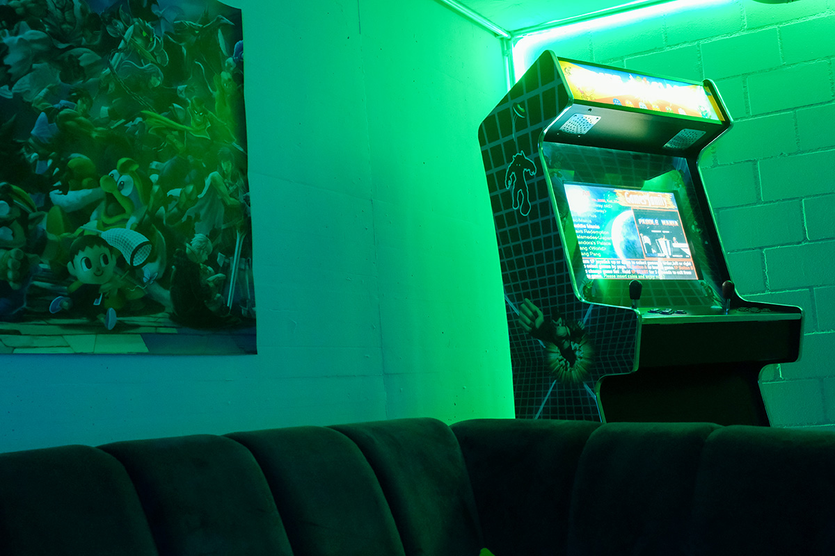 Spielautomat mit Joystick und einem Sofa im Vordergrund im GameInn Allegra Lodge.