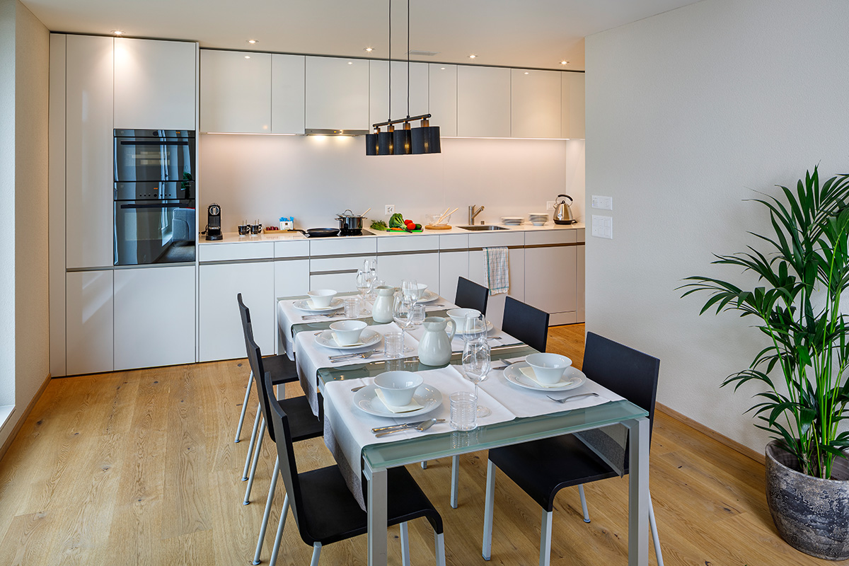 Moderner Wohn- und Essbereich im achesa ShareLiving im Hotel Allegra Lodge in Kloten: Offener Grundriss mit voll ausgestatteter Küche und grossem Esstisch für Co-Living Bewohner in der Region Zürich-Flughafen.